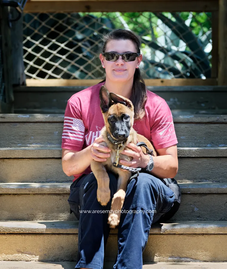 Yasmin sitting on the steps with a young Malinois puppy